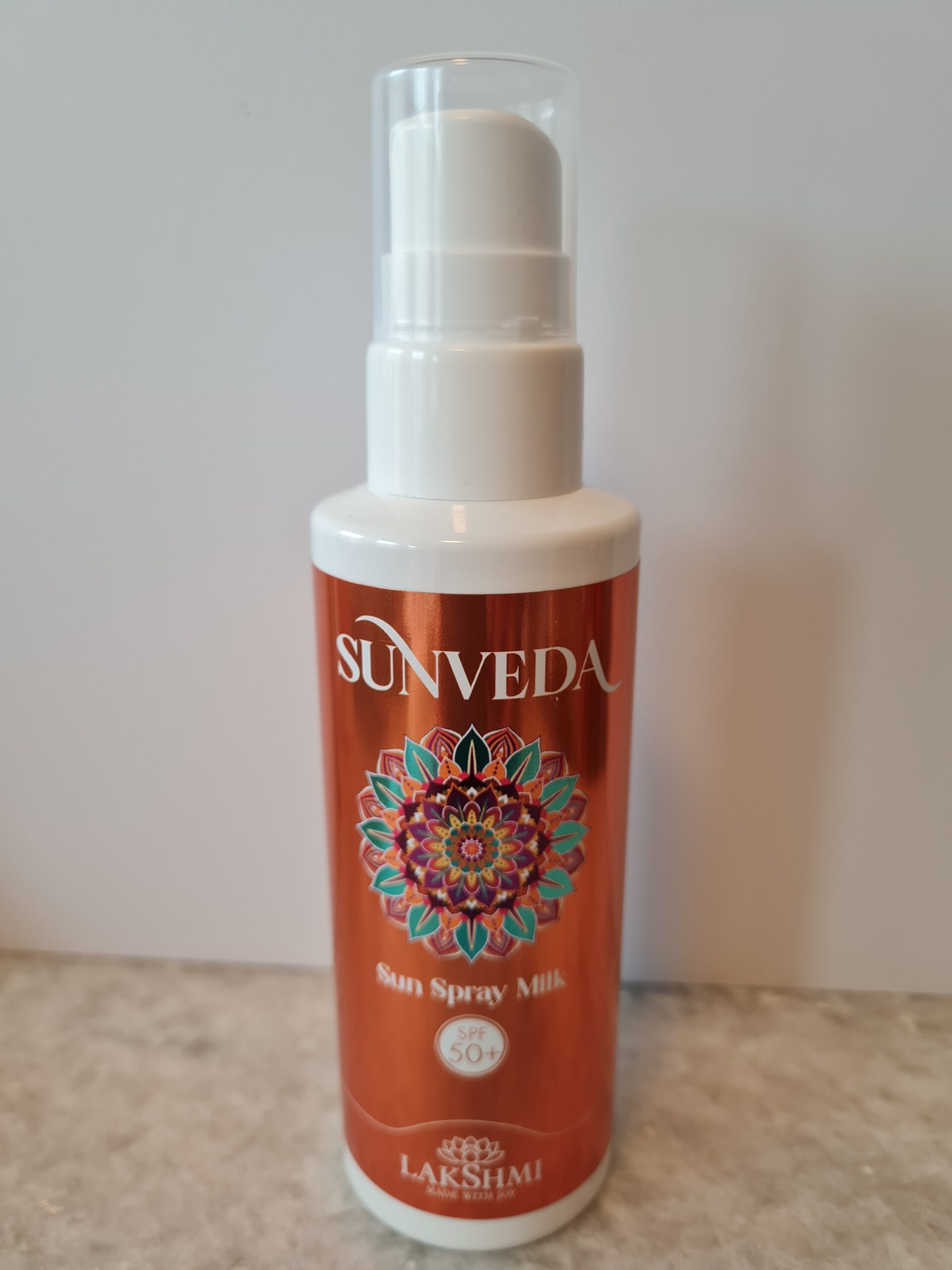 Sunveda Sun Spray Milk bottle with white pump and cap, red label and colorful mandala design on the front.